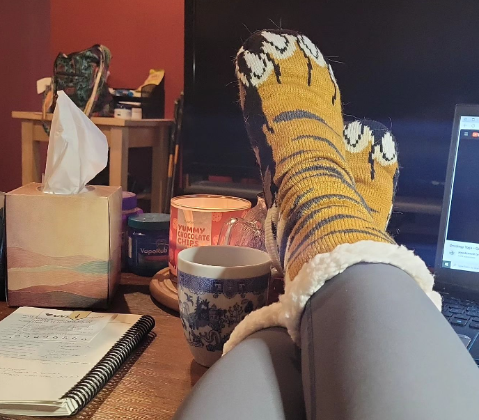 Feet wearing tiger socks on a table with a cup of tea and a chocolate chip candle.